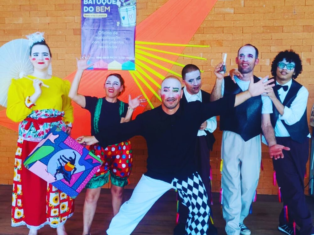 Atores da Cia de Teatro Novo Olhar com máscaras e figurinos coloridos ao lado do grupo Batuque do Bem