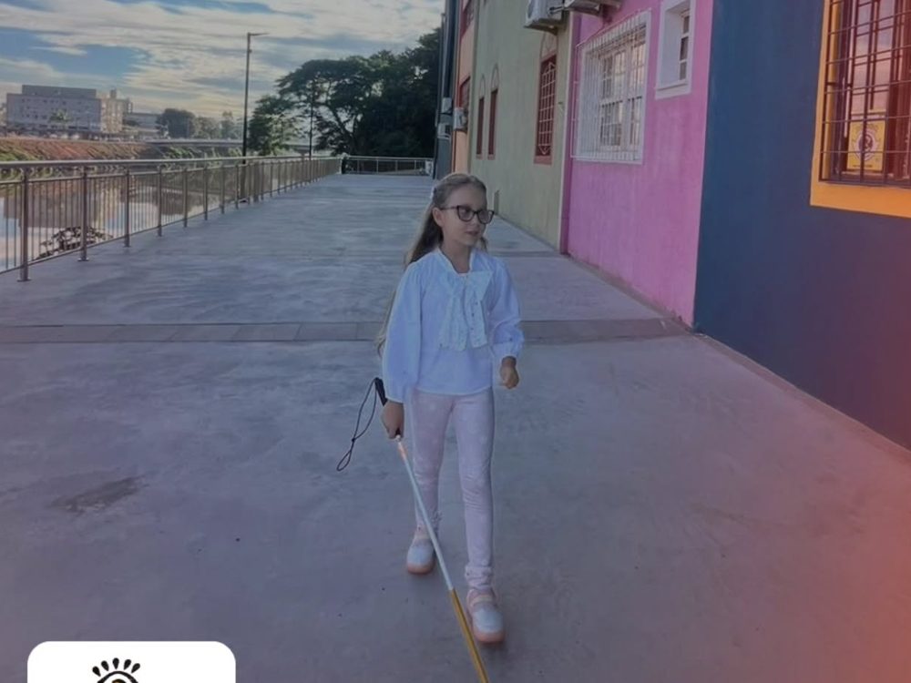 Aluna com bengala branca caminhando sozinha por uma calçada de Tubarão