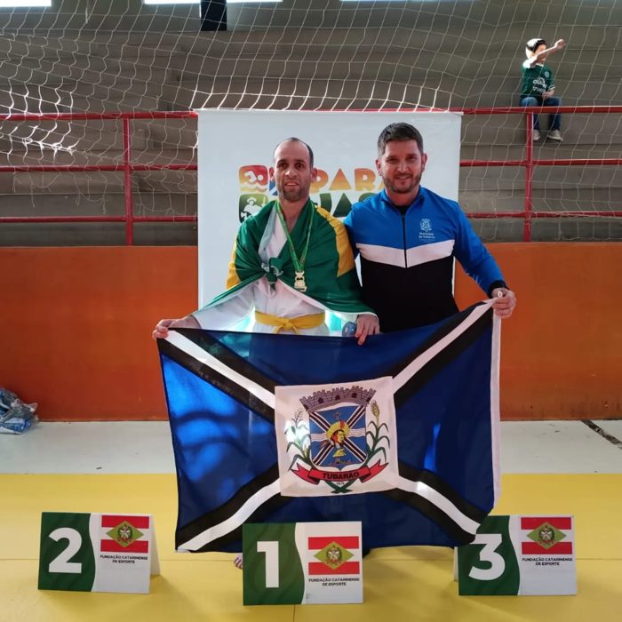Pedrinho e o treinador João no pódio com a bandeira de Tubarão, ouro no judô