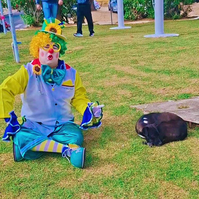 Palhaço Marmita deitado na grama ao lado de um cachorro, após um dia de ação com a ATIDEV