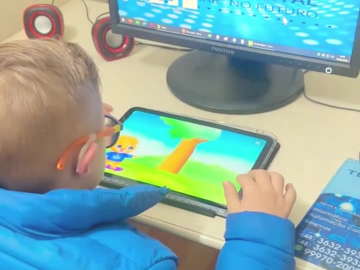 Criança com fones de ouvido usando um tablet na sala de informática da ATIDEV